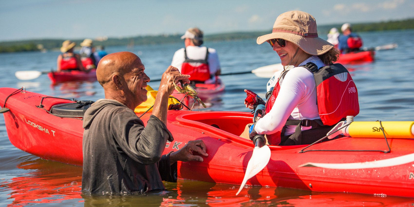 A local Cuban guide holding up a grab to a woman in a sea kayak